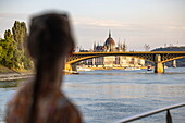 Ungarisches Parlamentsgebäude an der Donau, gesehen von Flusskreuzfahrtschiff Viktoria (nicko cruises) mit der Silhouette einer Frau im Vordergrund, Budapest, Pest, Ungarn, Europa