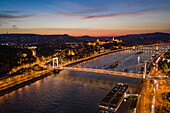 Luftaufnahme von Flusskreuzfahrtschiffen, die an der Donau liegen, mit Brücken, Budaer Burg und Fischerbastei in der Abenddämmerung, Budapest, Pest, Ungarn, Europa