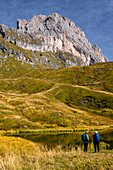 Hikers in front of a lake in front of the Odlegruppe, Seceda in autumn, Val Gardena, Bolzano, South Tyrol, Italy
