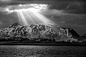 Sunrays shine through hole in the clouds onto mountains and fjord, Skreda, Lofoten, Nordland, Norway