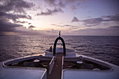 Couple in the Crow&#39;s Nest on the bow of the expedition cruise ship SH Diana (Swan Hellenic) with Aldabra on the horizon at dusk, at sea, near Seychelles, Indian Ocean 