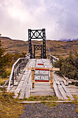  Vertical image of old bridge in Torres del Paine National Park, forbidden by &quot;no pasar&quot;, highlights abandoned atmosphere and conservation of wild nature, Chile, South America 