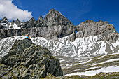 Mann und Frau beim Wandern sitzen auf Felsblock und blicken auf Tschingelhörner mit Martinsloch, Plaun Segnas Sut, Unterer Segnesboden, Tektonikarena Sardona, Glarner Hauptüberschiebung, UNESCO Weltnaturerbe Glarner Alpen, Glarner Alpen, Graubünden, Schweiz 