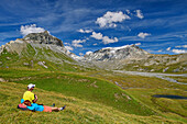  Man and woman hiking sitting in meadow and looking at Atlas and Trinserhorn, Oberer Segnesboden, Tectonic Arena Sardona, Glarus thrust, UNESCO World Natural Heritage Glarus Alps, Glarus Alps, Graubünden, Switzerland  