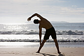  Man doing stretching exercises on Bombinhas beach, Santa Catarina, Brazil 