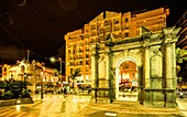  Triumphal arch in the Plaza de los Reyes with a view of a cafe and the Casa de los Dragones in the evening, Ceuta, Strait of Gibraltar, Spain 