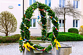 mit Girlanden aus Buchszweigen und bunten Ostereiern geschmückter Osterbrunnen vor der Alten Schule in Forstinning in Oberbayern in Deutschland