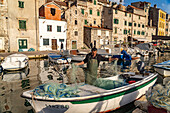 Fischer mit Netz auf seinem Boot im kleinen Hafen in der Altstadt von Sibenik, Kroatien, Europa