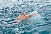 Erklimmen eines Eisbergs beim Baden in arktischen Gewaessern, Spitzbergen, Svalbard, Norwegen, Arktis