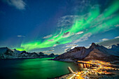 Polarlichter über der beleuchteten Ortschaft Mefjordvaer am Mefjord, Mefjordvaer, Senja, Troms, Norwegen