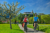 Mann und Frau beim Radfahren mit Schloss Hohenaschau im Hintergrund, Hohenaschau, Bodensee-Königssee-Radweg, Oberbayern, Bayern, Deutschland