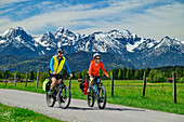 Mann und Frau fahren auf dem Bodensee-Königssee-Radweg mit Tannheimer Bergen im Hintergrund, Schwangau, Allgäu, Schwaben, Bayern, Deutschland