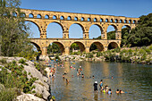 Menschen baden im Fluss Gardon und Kanus am römischen Aquädukt Pont du Gard, UNESCO Welterbe in Vers-Pont-du-Gard, Frankreich, Europa