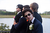 Young boy in sunglasses and suit facing camera with three friends, also in suits, in background