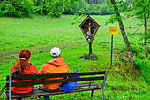  Man and woman taking a break on a bench, wayside cross in the background, Via paradiso, Millstätter See, Nockberge, Niedere Tauern, Carinthia, Austria 