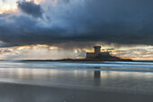  La Rocco Tower stands on the sandy beach at sunset. The sky is reflected in the water. 