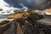  View of the path and the rocky island of San Juan de Gaztelugatxe under dark clouds. 