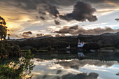 Blick über Fluß auf die Kirche Iglesia Parroquia de Nuestra Señora de los Dolores am Jakobsweg bei Sonnenuntergang, Barro, Llanes, Asturien, Spanien