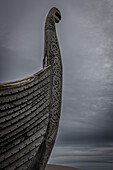  Bow of old Viking ship with dragon head against grey sky. 