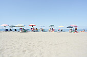 Eine Gruppe von Menschen in einer Reihe am Strand, mit Blick auf das ruhige Wasser, im Hintergrund ein zarter Morgenhimmel in sanften Pastelltönen, Kampanien, Italien, Europa