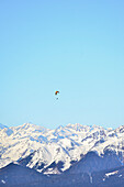 Gleitschirmflieger schwebt über dem Gipfel des K2 vor einem türkisfarbenen, pastellfarbenen Himmel.