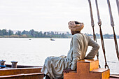 Member of the crew sitting at the prow of a dahabeah, passenger river boat of the Lazuli fleet, sailing on the Nile river, Egypt, northeast Africa