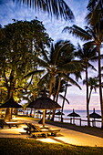 Liegestühle am Strand mit Kokospalmen bei Sonnenuntergang im Royal Palms Beachcomber Resorts, Grand Baie, Rivière du Rempart, Insel Mauritius, Indischer Ozean