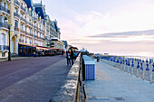 Strandpromende (Promenade Marcel Proust) mit Grand Hotel (Le Grand Hôtel) und Casino, Badehäuschen, Sonnenschirme am Strand bei Sonnenuntergang im Abendlicht in Cabourg an der Blumenküste (Côte Fleurie, Cote Fleurie) im Département Calvados in der Region Normandie in Frankreich