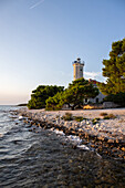 Insel Vir, Leuchtturm und Pinienwald mit Blick über die Küste auf das Gebäude und den Sonnenuntergang, Dalmatien, Kroatien, Adria, Mittelmeer