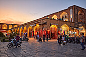 People walk in Naqsh-e Jahan Square illuminated at dusk. Isfahan, Iran.