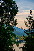  Panoramablick über ein Haus mit Turm am Luganersee mit Bergen und blauem Himmel und Wolken im Sonnenuntergang in Caslano, Tessin, Schweiz. 