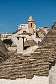  Trulli-Häuser mit der Kirche Santa Lucia im Hintergrund in Alberobello, Apulien, Italien. 