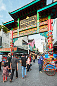 People walk through elaborate entrance gate to Kentandan District at the corner of Malioboro and Ketandan Wetan streets. Yogyakarta, Java, Indonesia.