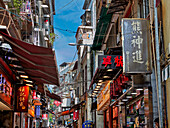  Alte Häuser mit zahlreichen Geschäften in der Rua de S. Paulo, einer schmalen Fußgängerzone, die zu den Ruinen der St. Pauls-Kirche führt. Macau, China. 