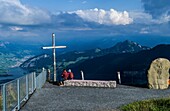  Evening mood on the Rigi, couple under a summit cross, boulder from the partner mountain Emei Shan (China), view of Lauerz and Lake Lauerz, Canton Lucerne, Switzerland 