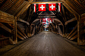 Inside the Old Historical Covered Wood Bridge Holzbrücke with Flags over River Aare at Night in Olten, Canton Solothurn, Switzerland.