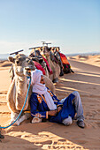  Camel driver with camels in the desert at sunset 