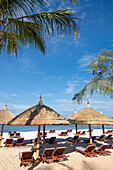 Loungers under thatched parasols on the beach at Vinpearl Resort. Phu Quoc island, Vietnam.