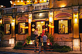 People stand at the Sakura Restaurant building illuminated at dusk. Hoi An Ancient Town, Quang Nam Province, Vietnam.