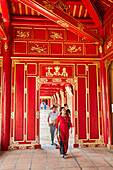 Tourists walk in the open gallery in Khon Thai Residence (Queen's Private Apartment) with vivid red painting. Imperial City, Hue, Vietnam.