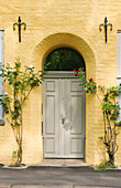  House entrance with climbing rose in front of yellow facade 