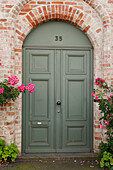  Green front door framed by climbing roses on brick house 