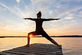  Woman doing yoga exercises on a jetty by the lake, warrior figure, Schleswig-Holstein, Germany 