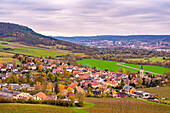  Idyllic village with colorful houses and church in hilly autumn landscape under cloudy sky, Kunitz, Thuringia, Germany 