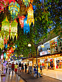 People walk in a narrow street brightly illuminated at night in Kusadasi, a large resort town on the Aegean coast of Aydin Province, Turkey.