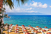 Rows of sunbeds under parasols on a sandy beach in Kusadasi, a large resort town on the Aegean coast of Aydin Province, Turkey.