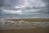 A cloudy sky over a deserted beach with wet sand and gentle waves.