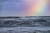 Ocean waves under a cloudy sky with a vibrant rainbow.