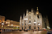 People walk in Duomo Square (Piazza del Duomo) in front of the Duomo Cathedral illuminated at night. Milan, Italy.