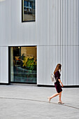 Frau in Pumps passiert modernes Gebäude im "Design District", Greenwich, London, England, Vereinigtes Königreich, UK, Europa